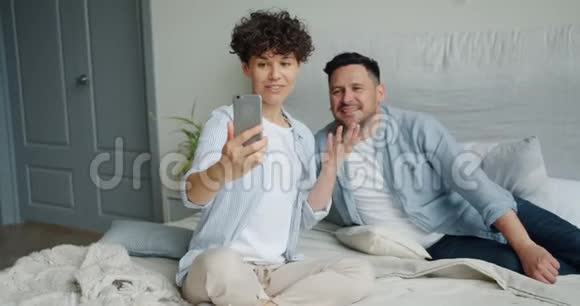 年轻夫妇用智能手机打视频电话在床上竖起大拇指视频的预览图