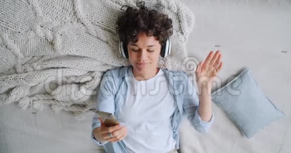 女孩躺在床上欣赏音乐耳机观看智能手机视频的预览图