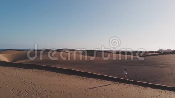 空中景色是一个美丽的年轻女子沿着沙丘散步的侧景日落或日出的黄金时刻视频的预览图