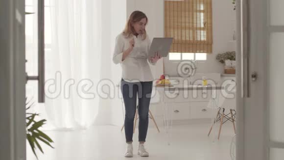 漂亮的白人女孩从笔记本电脑上得到好消息然后跳起来开朗的年轻女性在网上交流视频的预览图