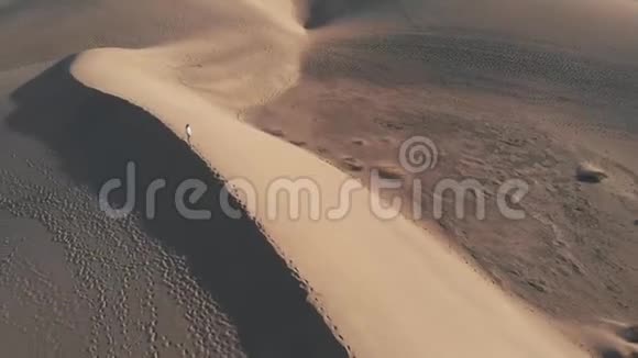 鸟瞰一个美丽的女孩站在沙丘上日落或日出在沙漠上空高速飞行的无人机视频的预览图