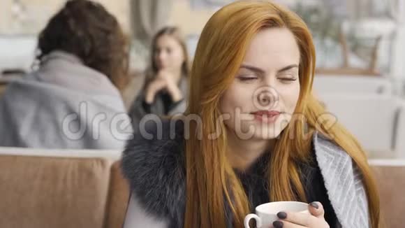 可爱的年轻白种人女人被毯子覆盖喝茶或咖啡坐在露台上的桌子上女孩视频的预览图