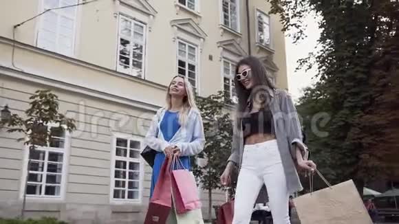 迷人的无忧无虑的女人带着各种各样的购物袋走在城市的街道上视频的预览图