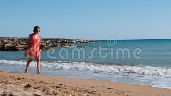 年轻迷人的女孩穿着红色短裙沿着大海散步白人黑发女人走在沙滩上穿红色衣服的年轻女孩视频的预览图