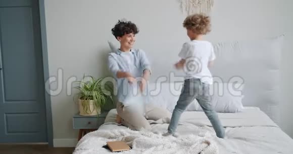 年轻女子和小男孩在公寓的床上享受枕头大战视频的预览图