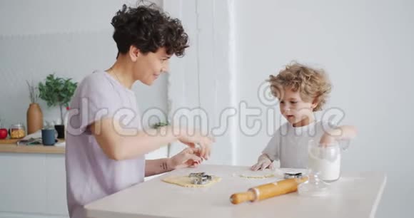 年轻的女人和小男孩把面粉放在面团上然后在厨房里玩得开心视频的预览图