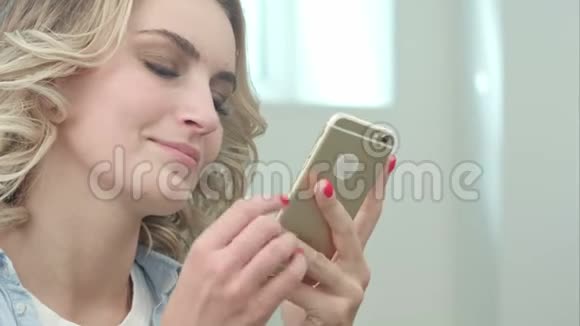 快乐的金发女郎坐在美容院里用智能手机视频的预览图