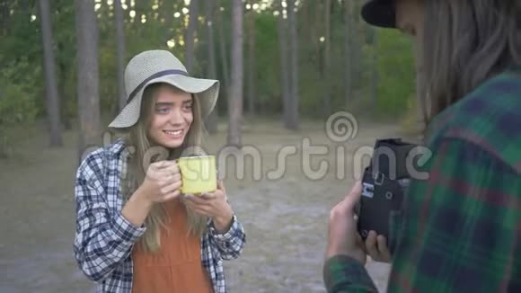 年轻漂亮的白种人女人在森林的背景上摆着黄色的杯子男朋友给他拍照视频的预览图