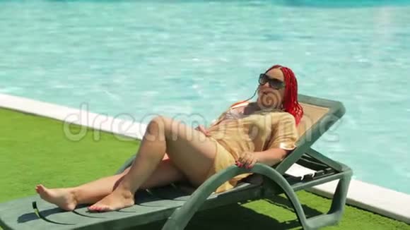 一个年轻的黑发女人正在游泳池附近的一张躺椅上晒太阳视频的预览图