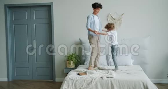 快乐的女人在床上跳着可爱的小儿子牵着手然后拥抱着视频的预览图