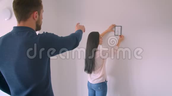 白种人黑发女孩挂在白墙上的相框照片而她的男朋友命令正确的地方视频的预览图