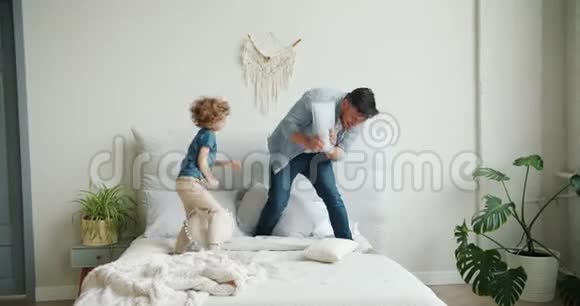 父亲和儿子在床上玩耍打着枕头然后妈妈回家了视频的预览图