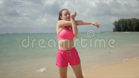 穿着粉色运动服的冷静的女人在沙滩上伸着脖子视频的预览图