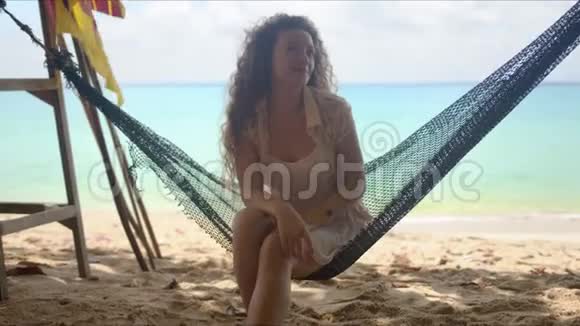 站在沙滩吊床上摆手的微笑女人视频的预览图