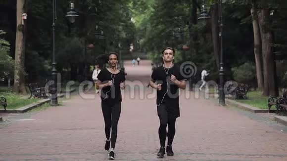 年轻的白种人男子和戴着慢跑服戴着耳机的穆斯林女孩在公园里跑步理念是健康的生活方式视频的预览图