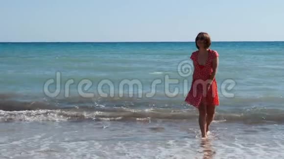 穿着红色短裙带着牙套的白种人女孩沿着海滩散步美丽的女孩在沙滩上玩得开心和微笑视频的预览图