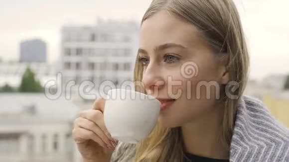 描绘了一个年轻的白种人女人她被毯子覆盖喝着茶或咖啡女孩望着一边享受她的饮料视频的预览图