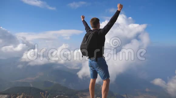 年轻的男性徒步旅行者爬上山顶举起手臂在夏季旅行中享受自由的人多云的天空视频的预览图
