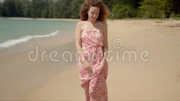 阳光明媚的日子里一个穿着花裙子在沙滩上散步的好女人视频的预览图