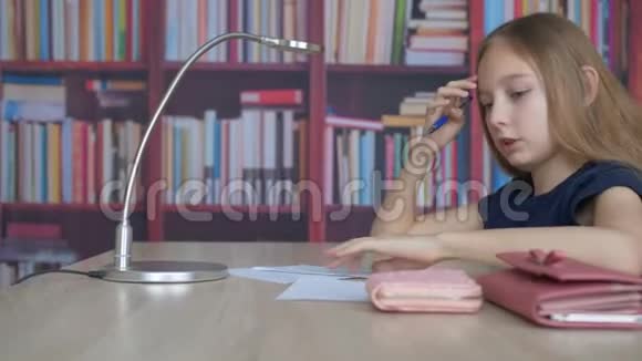 学生女孩用钢笔在书柜背景的纸上写字在家里办公室做家庭作业的少女视频的预览图