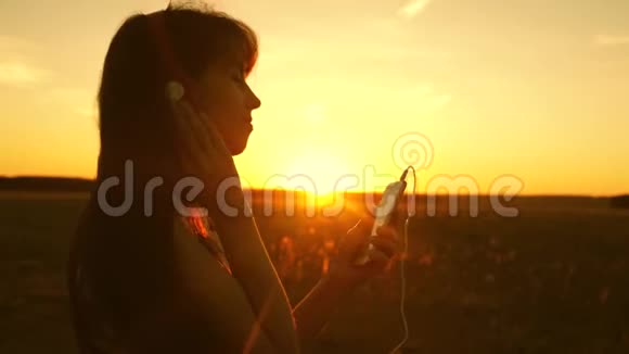 女孩在日落的光线中旅行和听音乐和舞蹈戴着耳机和智能手机的年轻女孩视频的预览图