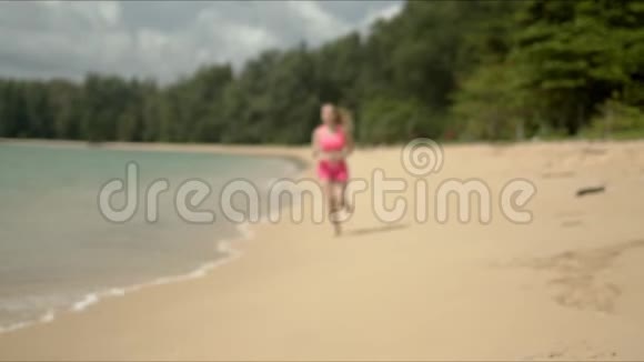 穿着粉红色运动服的可爱女人在海滩上奔跑视频的预览图