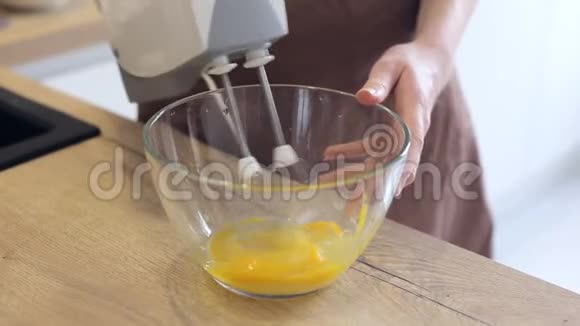 穿围裙的女人在碗里用搅拌机打鸡蛋视频的预览图