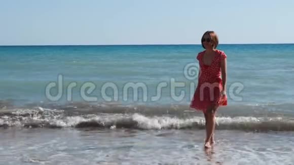 穿着红色短裙带着牙套的白种人女孩沿着海滩散步美丽的女孩在沙滩上玩得开心和微笑视频的预览图