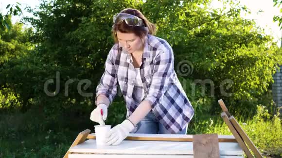 成人手工艺妇女在夏季果园里用白色油漆画木木板视频的预览图