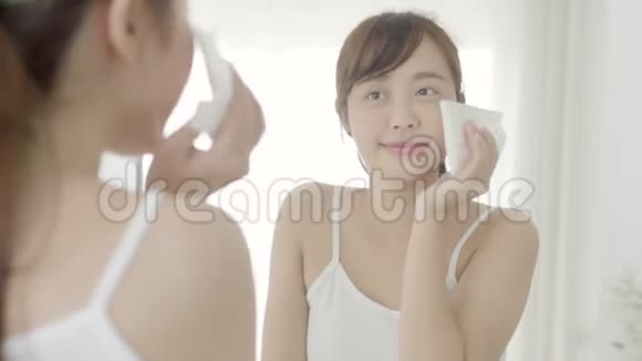 美丽的肖像年轻的亚洲女人微笑和喜悦与皮肤护理使用油抹纸脸上的镜子在浴室视频的预览图