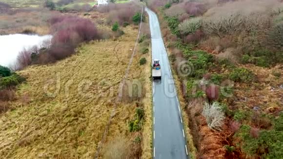 爱尔兰农村公路上拖拉机和拖车驾驶的鸟瞰图视频的预览图