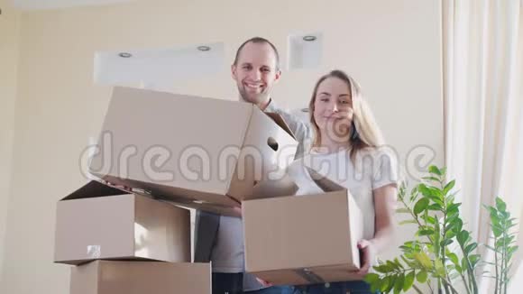 一对幸福的年轻夫妇带着纸板箱在他们的新房子里视频的预览图