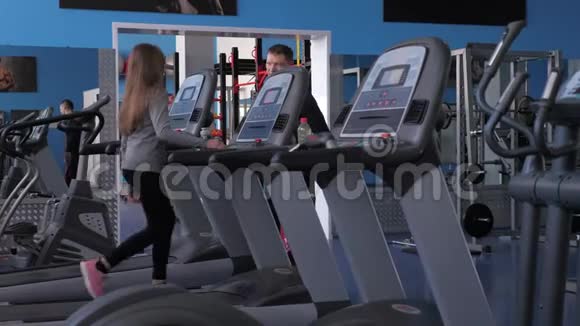 女孩在教练的监督下在跑步机上训练行走时加强腿部肌肉有氧运动负荷视频的预览图