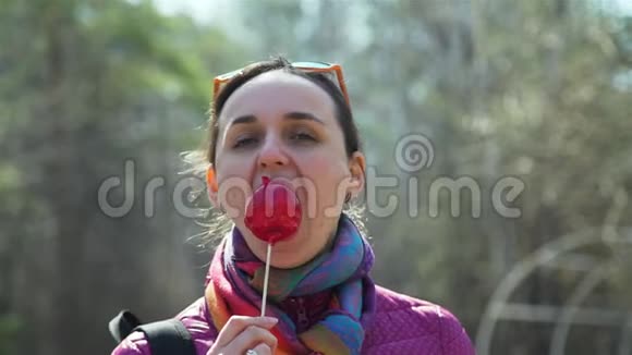 在公园里吃焦糖红苹果的年轻女人视频的预览图