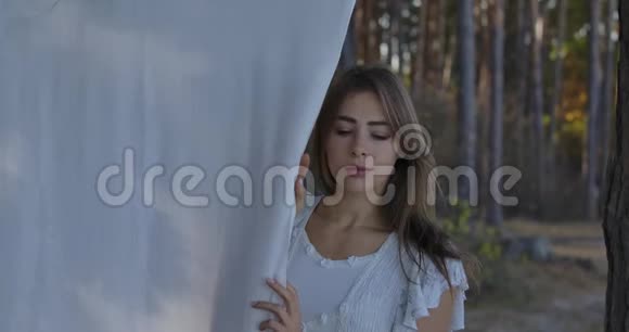一位年轻美丽的高加索女人站在森林里环顾四周的肖像穿着白色衣服的漂亮女孩视频的预览图