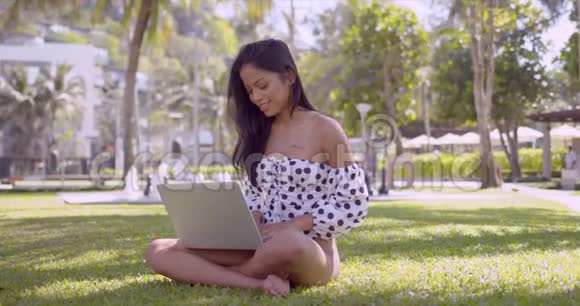 一个聪明的亚洲女人坐在公园草地上用笔记本电脑打字视频的预览图