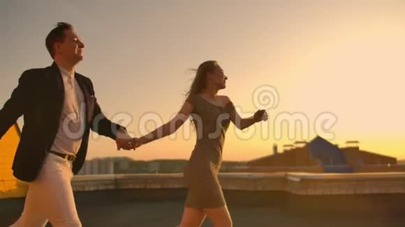 一个男人和一个女人在屋顶上奔跑手牵着手屋顶上的慢动作爱好者视频的预览图