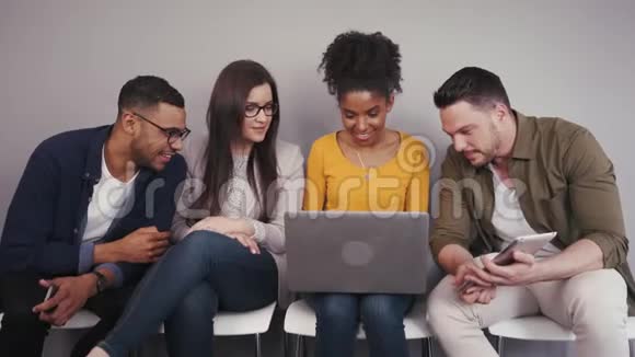 一群不同的年轻人朋友坐着看着一台笔记本电脑在室内一起工作视频的预览图