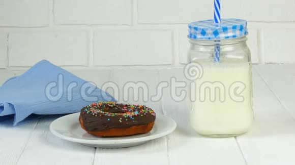 在一罐牛奶和一罐蓝色的砖墙旁边白色盘子上有彩色粉末的大巧克力甜甜圈视频的预览图