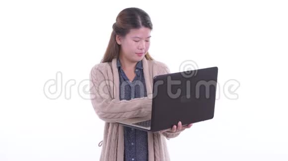 快乐的年轻亚洲女人一边思考一边用笔记本电脑准备冬天视频的预览图