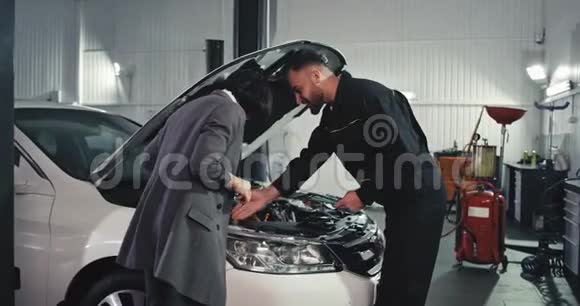 汽车修理工男和一个年轻的女工程师分析了发动机的问题他们有一个友好的视频的预览图