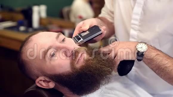 理发店里坐在美发椅上的胡子拉碴客户用电动剃须刀剪脸视频的预览图