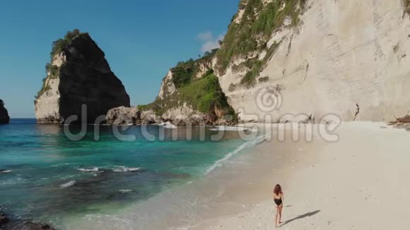 后景女子比基尼漫步在海滩与海石和绿松石海洋蓝天努萨佩奈达Atuh海滩视频的预览图