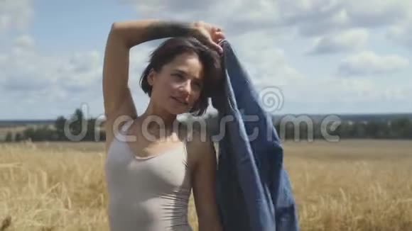 可爱的短发女人穿着紧身衣手上拿着牛仔裤夹克站在麦田上自信视频的预览图