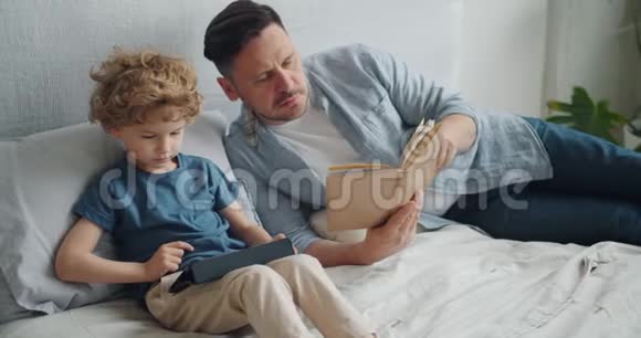 父亲儿子整天在床上一起看书看笔记本电脑上的卡通视频的预览图