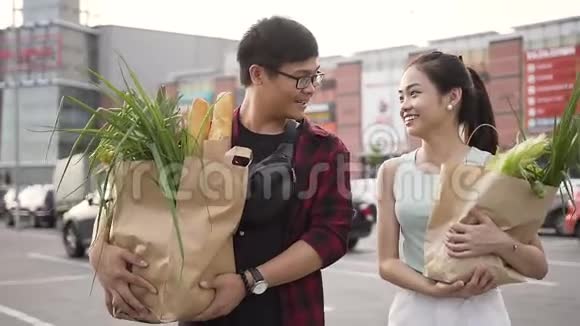 一对长相英俊笑容满面的越南夫妇带着装满各种食物的袋子从超市出发视频的预览图