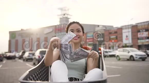 迷人的照片微笑满意的亚洲女人撒钱坐在购物车视频的预览图