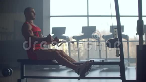 一个年轻人在健身俱乐部里背着力量锻炼机锻炼身体在运动健将后面做运动视频的预览图