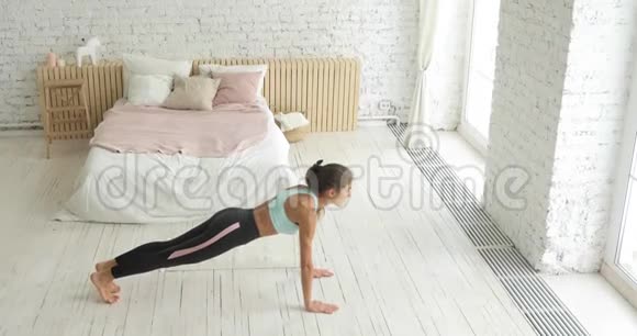 年轻的运动女性在运动中做木板腹肌在家里侧面看视频的预览图