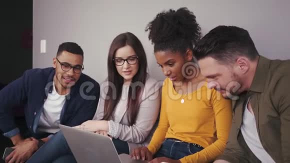 一群混血朋友坐在现代化的办公室里看着一台笔记本电脑作为一个团队一起工作视频的预览图